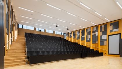 Großer Hörsaal mit dunklen Sitzen und Hanf-Akustikpaneelen an den holzverkleideten Wänden