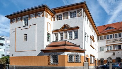 Detailreiche Jugendstilfassade des Dorotheum Linz mit aufwendig verzierten Fenstern, geometrischen Ornamenten und markanten orangefarbenen Zierelementen, restauriert mit Histolith-Farben