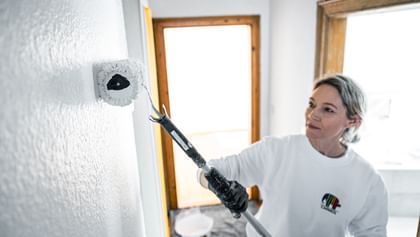 Malerin, die mit einem Farbrolle eine weiße Wand streicht