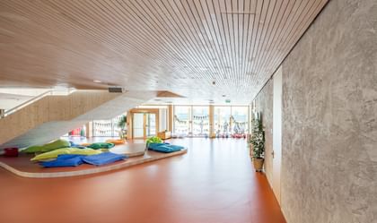 Ein Raum in einer Volkshochschule. Im Vordergrund sind bunte Sitzkissen in verschiedenen Farben (grün, blau) auf einem hellen Boden angeordnet. Auf der linken Seite ist eine Treppe, die zu einem oberen Bereich führt.