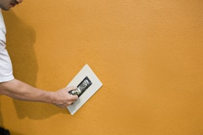 Hand streicht Putz auf Fassade – Schutz und Schönheit in einem Arbeitsschritt