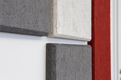 Nahaufnahme strukturierter Hanfpaneele in Grau und Beige an weißer Wand mit rotem Akzent
