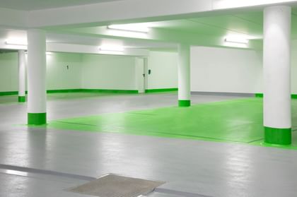 Ein leeres Parkhaus mit grauem Boden und weißen Wänden. Die Säulen sind im unteren Bereich grün gestrichen und der Boden ist in einem Bereich grün markiert.