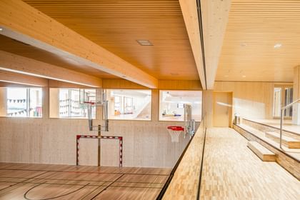 Sporthalle einer Volkshochschule mit einem Fußballtor, einem Basketballkorb und einer Tribüne aus Holz.