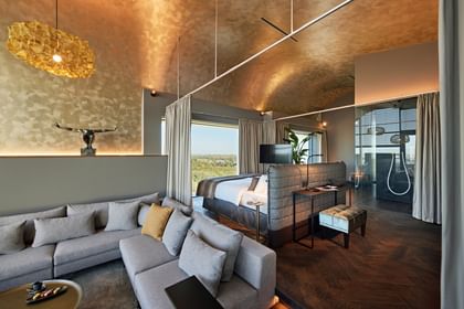 Großes Hotelzimmer mit einer goldenen Decke, grauer Couch und Bett