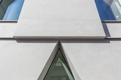 Nahaufnahme Fassade eines mehrstöckigen weißen Gebäudes mit großen, schmalen Fenstern, die in einer einzigartigen, spitz zulaufenden Form angeordnet sind