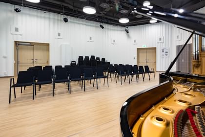 Kleiner Konzert- oder Vortragssaal in der Anton Bruckner Privatuniversität Linz mit aufgestellten Sesselreihen, einem schwarzen Flügel und klarer, moderner Raumgestaltung, vorbereitet für musikalische oder akademische Veranstaltungen.