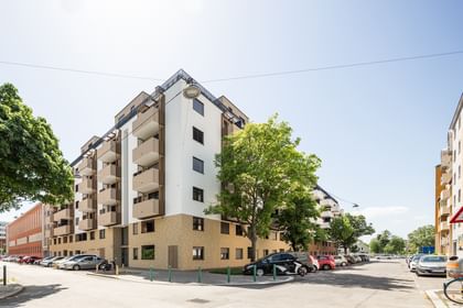 Außenansicht Mehrparteienhaus, Fassade in weiß und braun, davor eine Straßenkreuzung und parkende Autos