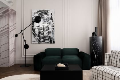 Eleganter Loungebereich einer Executive Suite im „The Amauris“ Wien mit tiefgrünem Samtsofa, großem abstraktem Schwarz-Weiß-Gemälde, skulpturaler schwarzer Stehleuchte, schwarzem Marmorsockel und bodenlangen beigefarbenen Vorhängen.