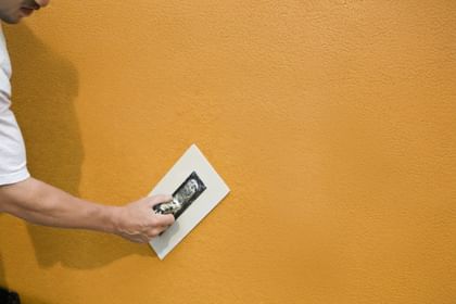 Hand streicht Putz auf Fassade – Schutz und Schönheit in einem Arbeitsschritt