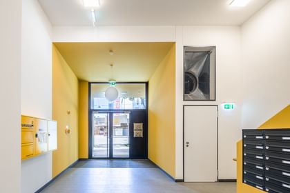 Eingangsbereich Mehrparteienwohnung mit Treppe, gelber Stiege, weißen Wänden Eingangstüre