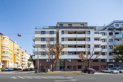 Totalansicht Mehrparteienhaus, Fassade in Klinkeroptik, davor geparkte Autos und Bäume