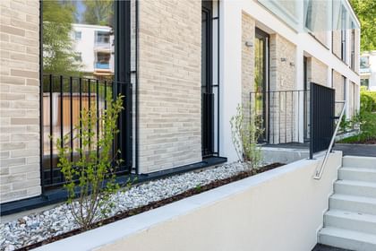 Detail der hellen Klinkerfassade mit schlanken Fenstern und frischem Grün im Eingangsbereich