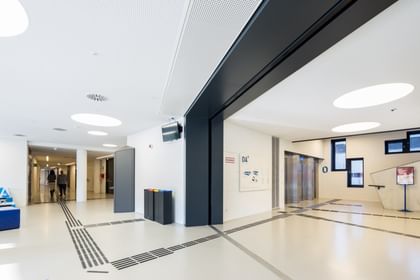 Minimalistischer, heller Korridor im Erdgeschoss der Wirtschaftsuniversität Wien mit Aufzügen, weißen Wänden, dunklem Boden und moderner Beschilderung.