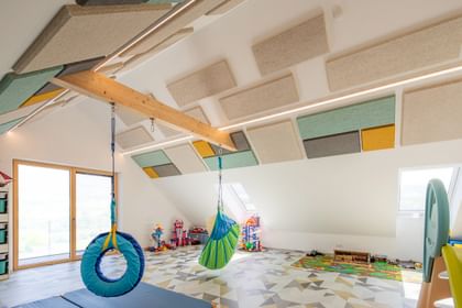 Spielzimmer mit Hängeelementen und bunten Akustikpaneelen unter der Dachschräge