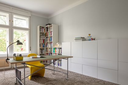 Arbeitszimmer mit Tisch, gelbem Arbeitsstuhl und weißem Bücherregal