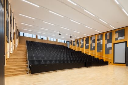 Großer Hörsaal mit dunklen Sitzen und Hanf-Akustikpaneelen an den holzverkleideten Wänden