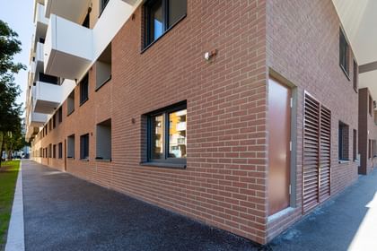 Außenansicht Mehrparteienhaus, Fassade in Klinkeroptik mit Fenstern, darüber weiße Balkone