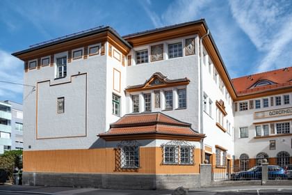 Detailreiche Jugendstilfassade des Dorotheum Linz mit aufwendig verzierten Fenstern, geometrischen Ornamenten und markanten orangefarbenen Zierelementen, restauriert mit Histolith-Farben