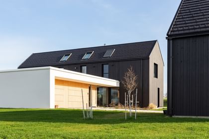 Blick auf die Garage in Tannenholz und das Wohngebäude mit dunkler Holzfassade