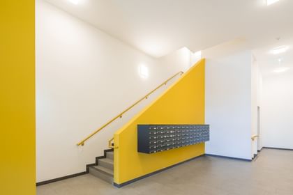 Eingangsbereich Mehrparteinenwohnung mit Treppe, gelber Stiege, weißen Wänden