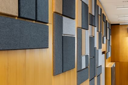 Holzwand mit geometrisch angeordneten Akustikpaneelen in verschiedenen Größen und Farben (Grau, Schwarz, Beige), gestaltet zur Schalloptimierung in der Uni Graz