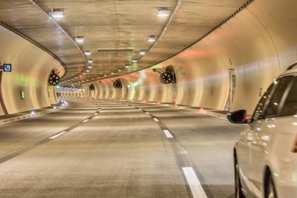 EinTunnel mit sanft geschwungenen Wänden, beleuchtet von bunten Lichtern und auf der rechten Seite ist ein Auto zu sehen, das in den Tunnel einfährt. 