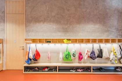 Eingangsbereich einer Schule. An der Wand hängen mehrere leuchtend gelbe und grüne Warnwesten und Rücksäcke auf Kleiderhaken. Darunter befindet sich ein offenes Regal, in dem Schuhe verstaut sind.