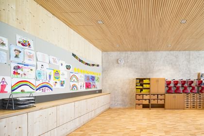 Klassenraum, an dessen Wand zahlreiche bunte Zeichnungen und Kunstwerke hängen, die von Kindern erstellt wurden.