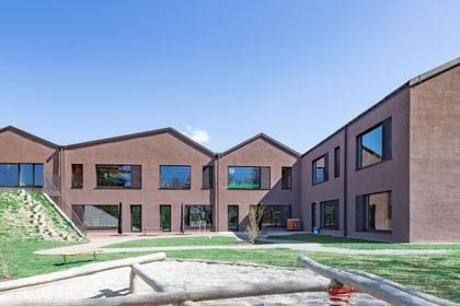 Zweistöckiges braunes Gebäude mit großen Fenstern und einem Spielplatz im Vordergrund