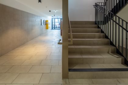 Eingangsbereich Mehrparteienhaus, langer Gang, Treppe mit schwarzem Geländer