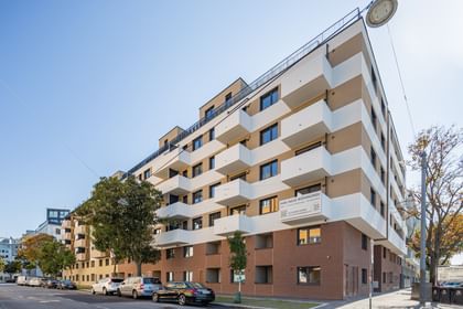 Außenansicht Mehrparteienhaus, Fassade in Klinkeroptik, weiße Balkone, davor geparkte Autos