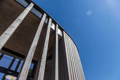 Holzfassade eines Gebäudes von unten. Man blickt auf einen blauen Himmel.