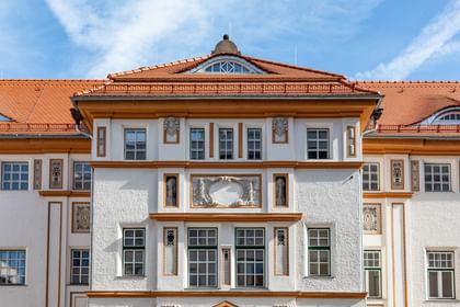 Detailreiche Jugendstilfassade des Dorotheum Linz mit aufwendig verzierten Fenstern, geometrischen Ornamenten und markanten orangefarbenen Zierelementen, restauriert mit Histolith-Farben