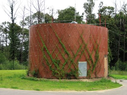Runder, orange-brauner Wassertank, der von grünen Pflanzen umwachsen ist.