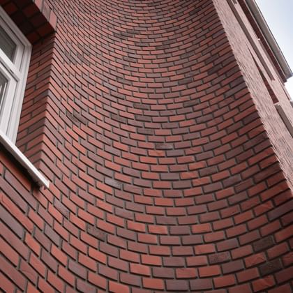 Backsteinfassade in leuchtendem Rotton mit schwungvoller Wölbung – kraftvoll und lebendig