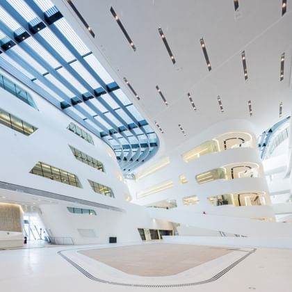 Weitläufiges, lichtdurchflutetes Atrium der Wirtschaftsuniversität Wien mit weißen Wänden, großen Fensterflächen und moderner Architektur.
