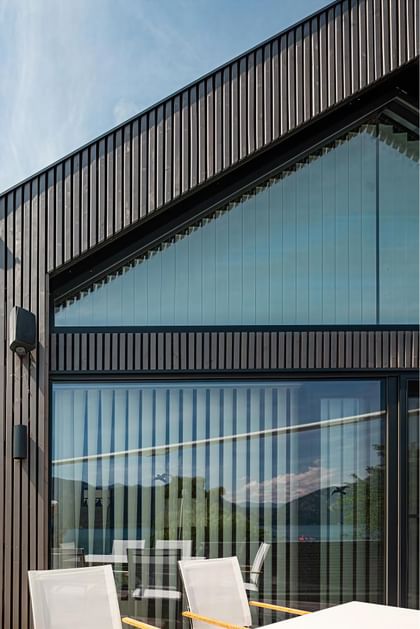 Großzügige Glasfront mit dunkler Holzfassade, Blick auf Berge und See