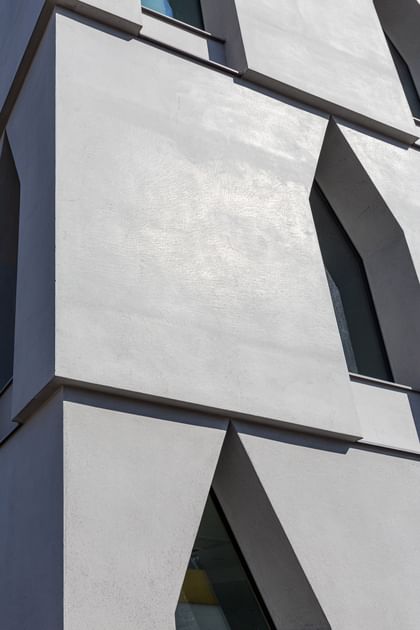 Fassade eines mehrstöckigen weißen Gebäudes mit großen, schmalen Fenstern, die in einer einzigartigen, spitz zulaufenden Form angeordnet sind