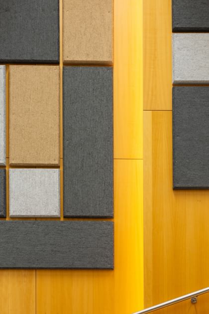 Holzwand mit geometrisch angeordneten Akustikpaneelen in verschiedenen Größen und Farben (Grau, Schwarz, Beige), gestaltet zur Schalloptimierung in der Uni Graz