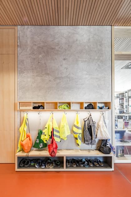 Eingangsbereich einer Schule. An der Wand hängen mehrere leuchtend gelbe und grüne Warnwesten und Rücksäcke auf Kleiderhaken. Darunter befindet sich ein offenes Regal, in dem Schuhe verstaut sind.