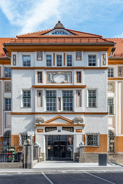 Detailreiche Jugendstilfassade des Dorotheum Linz mit aufwendig verzierten Fenstern, geometrischen Ornamenten und markanten orangefarbenen Zierelementen, restauriert mit Histolith-Farben