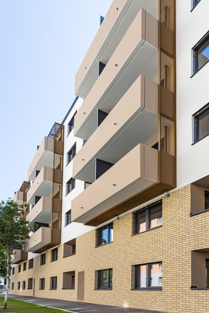 Nahaufnahme Fassade in beiger Klinkeroptik, mit Balkonen, davor Wiese
