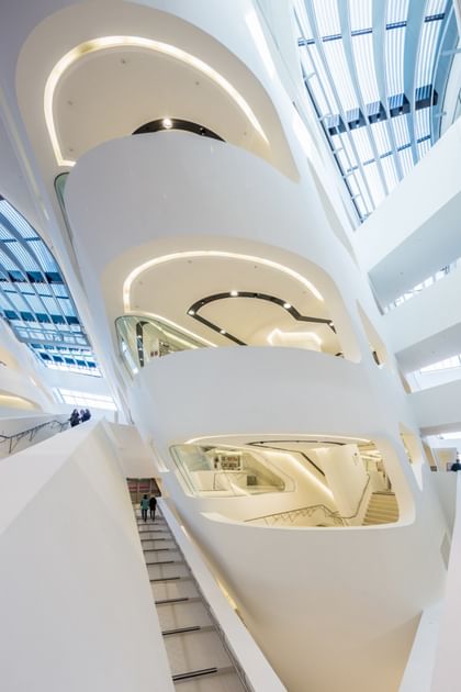 Detailaufnahme eines modernen Treppenaufgangs im Atrium der Wirtschaftsuniversität Wien mit weißen Wänden, runden Formen und viel Tageslicht.