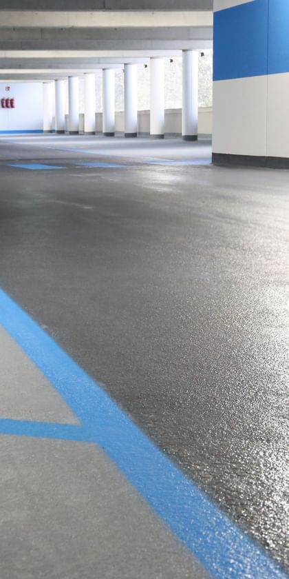 Grauer Boden einer Tiefgarage mit blauen Fahrbahn- und Parkmarkierungen