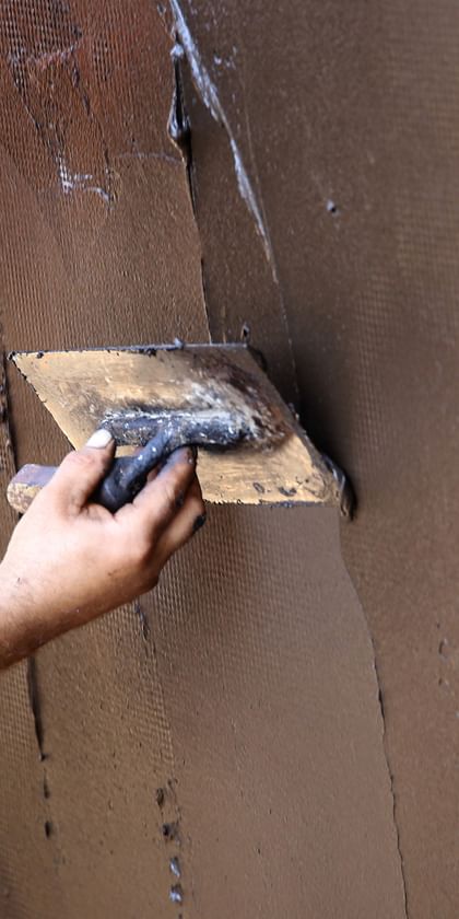 Ein Handwerker trägt braune Putzmasse auf eine Wand auf