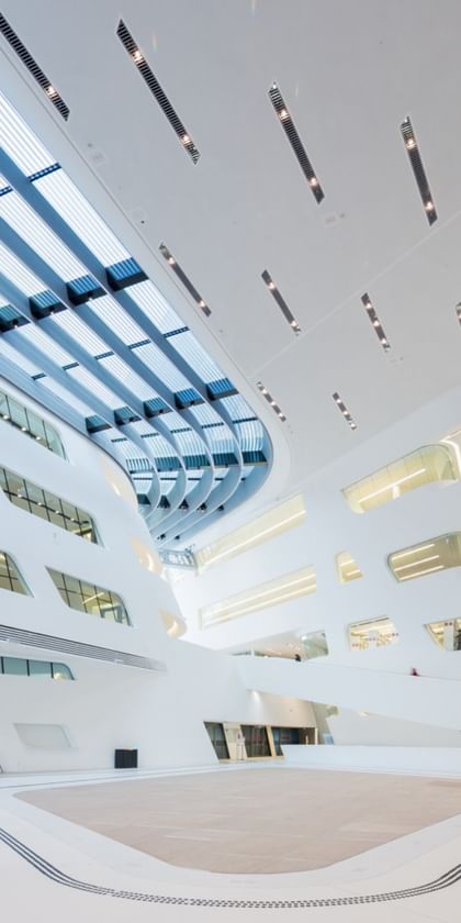 Weitläufiges, lichtdurchflutetes Atrium der Wirtschaftsuniversität Wien mit weißen Wänden, großen Fensterflächen und moderner Architektur.