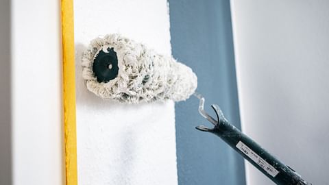 Farbroller, der eine blaue Wand weiß überstreicht