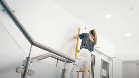 Handwerkerin misst Wandhöhe mit Wasserwaage, konzentriert bei der Montage