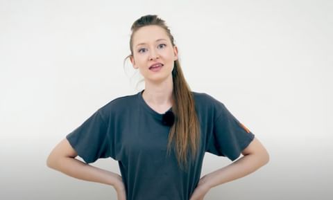 Junge Frau mit lockerem Pferdeschwanz erklärt vor weißer Wand mit lebendigem Blick